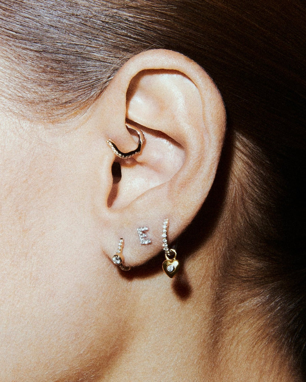 A styled ear with a gold clicker in the daith, diamond studs in the lobe and a gold heart-drop hoop.