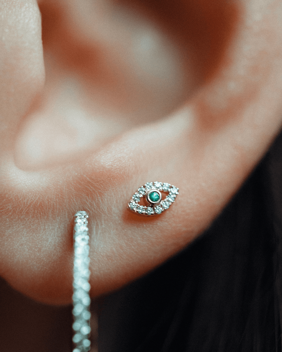 Eirene eye labret in 14k yellow gold, set with an emerald and natural diamonds, shown on the ear.