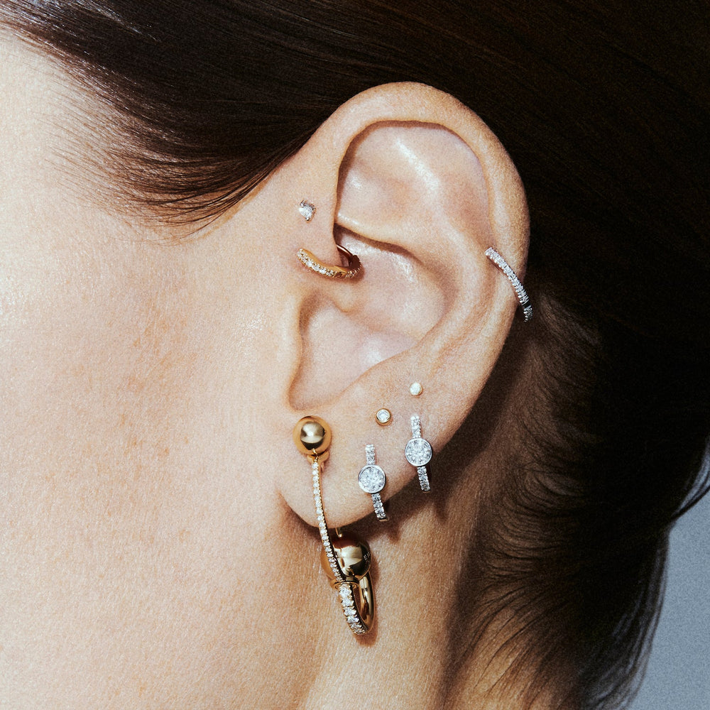 A stacked ear with a gold chain along the helix, a diamond ear cuff, lobe studs and a beaded gold drop hoop.